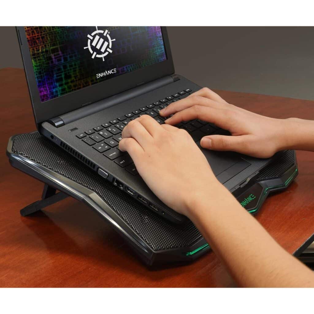 A person typing on a laptop placed on a cooling pad