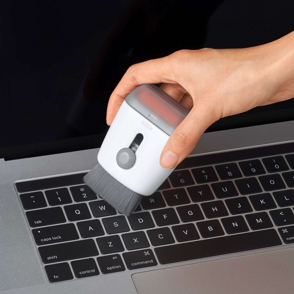 a person cleaning the laptop keyboard with a tool with brush