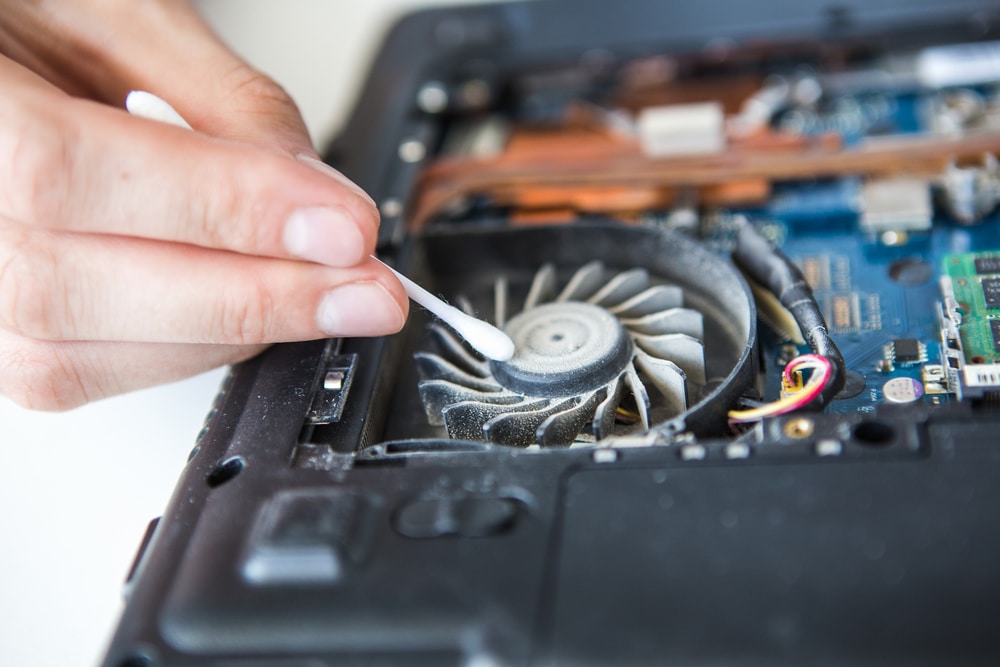 A close view of a person cleaning the laptop fan with a cotton swab