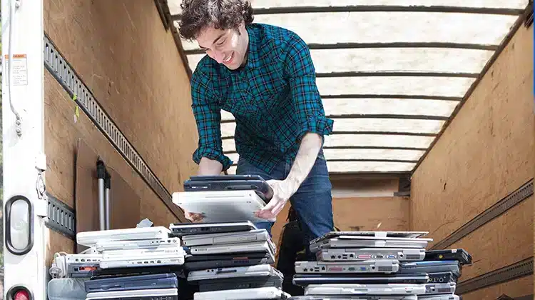 A view of a person placing laptops on a pile of old laptops