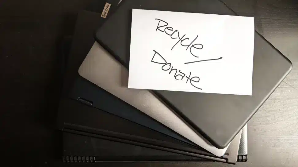 An overhead view of laptops with a paper on top saying recycle donate