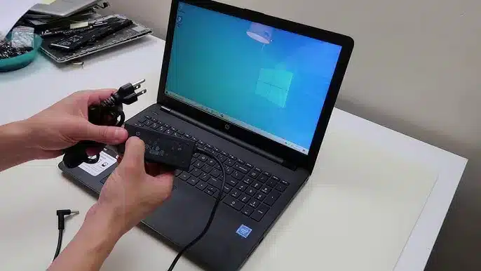 a person is holding a laptop charger along with the laptop on table